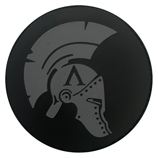 Black circular PVC patch with a gray Spartan Achilles helmet design on a plain white background