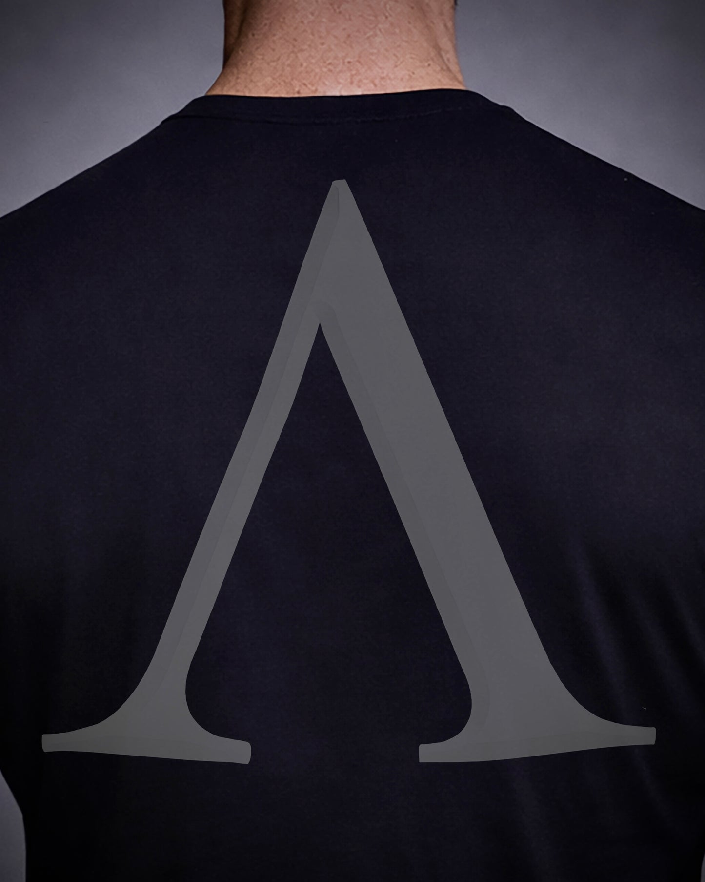 Close up of back view of man wearing black Achilles T-shirt printed with Large Lambda mark logo on back