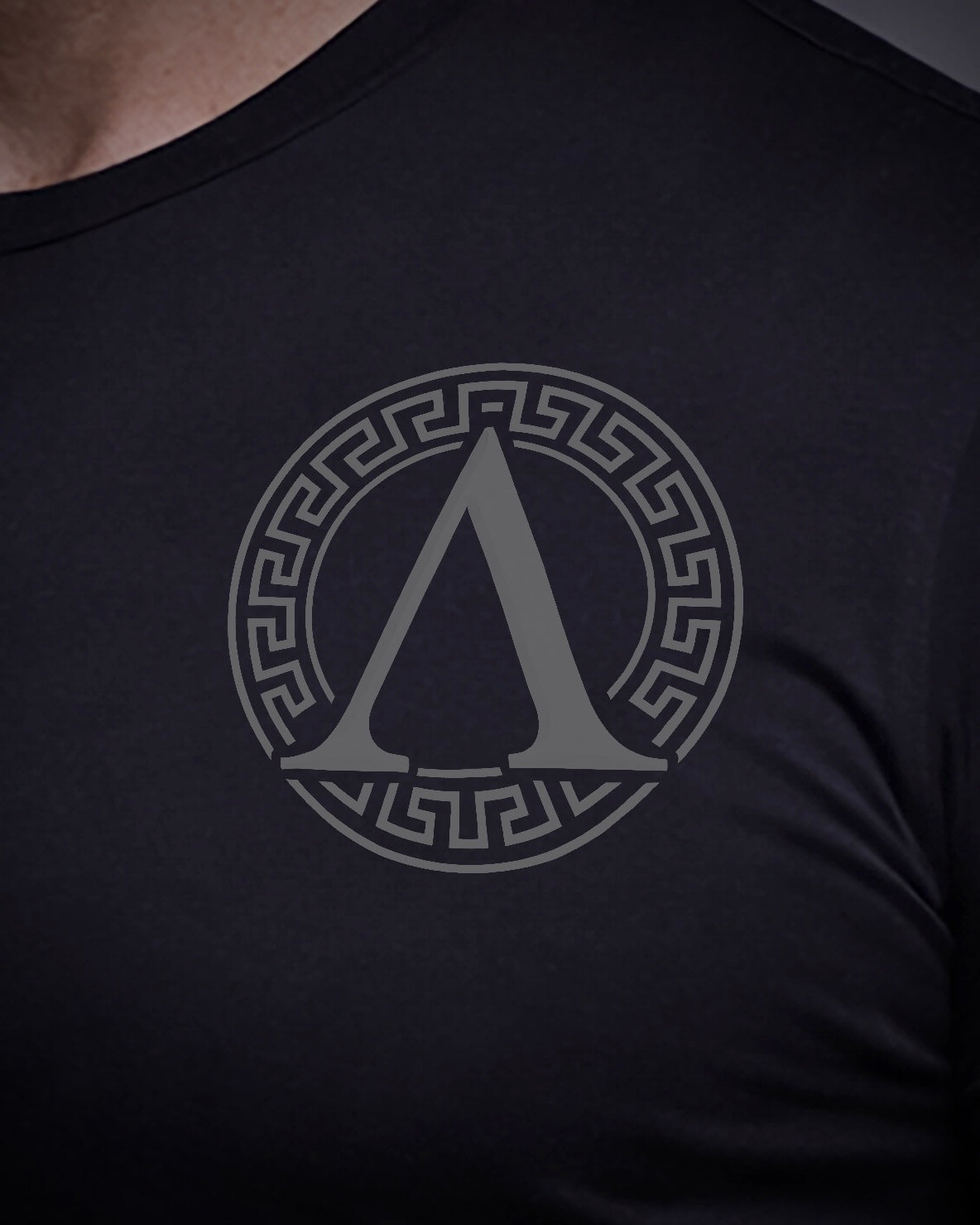 Close up of front view of man wearing black Achilles T-shirt printed with roundel logo on chest