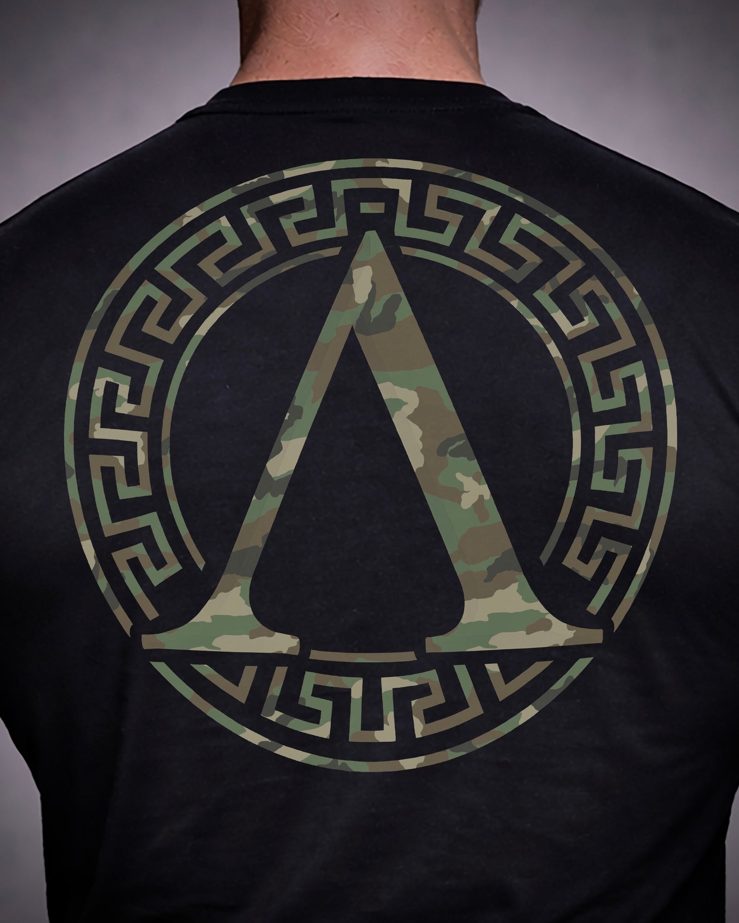 Close up of back view of man wearing black Achilles T-shirt printed with camouflage roundel logo on back
