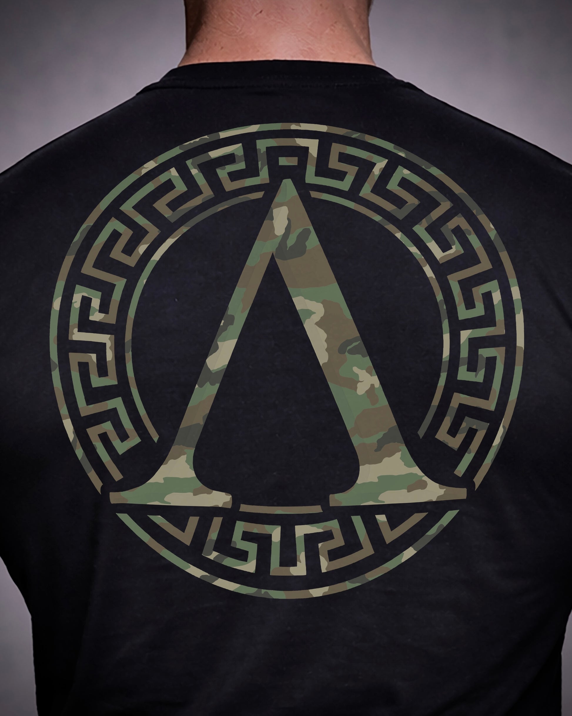 Close up of back view of man wearing black Achilles T-shirt printed with camouflage roundel logo on back