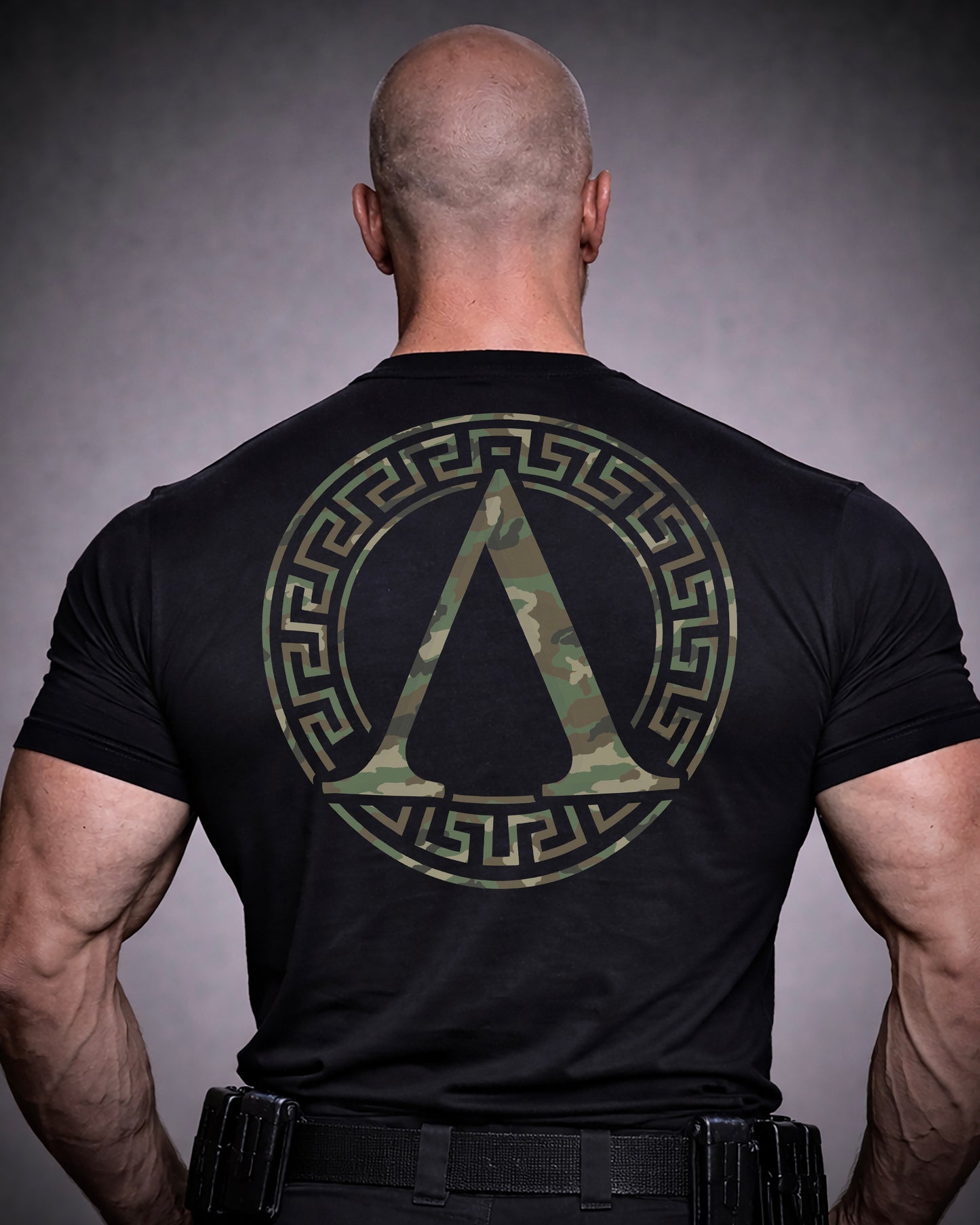 Back view of man wearing black Achilles T-shirt printed with camouflage roundel logo on back