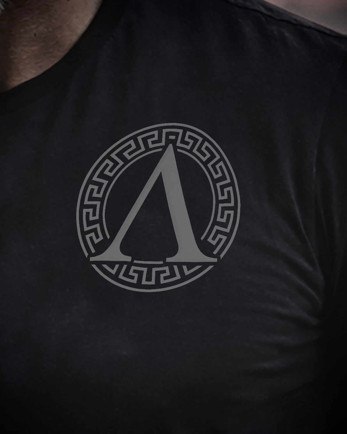 Close up of front view of man wearing black Achilles T-shirt printed with roundel on chest