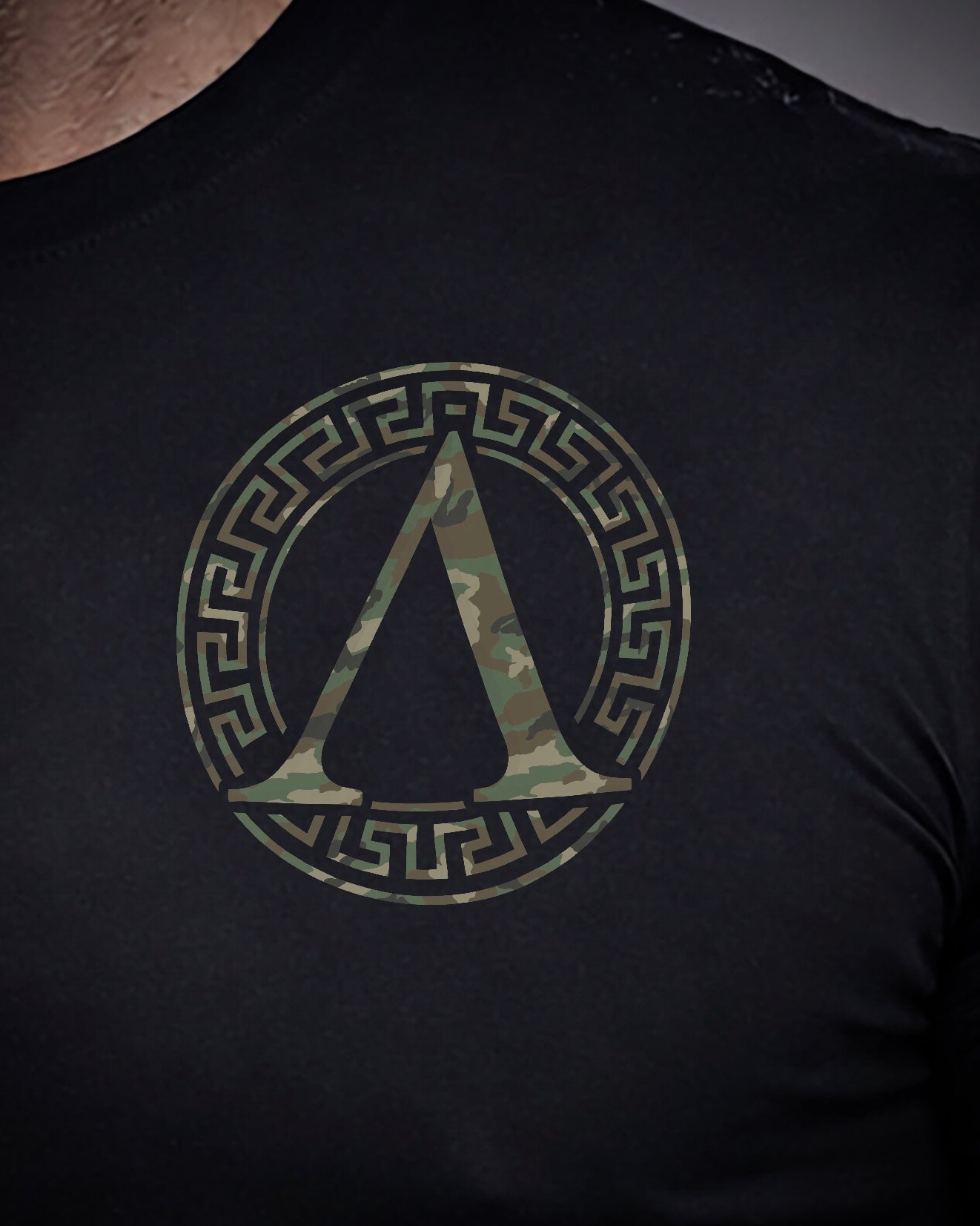 Close up of front view of man wearing black Achilles T-shirt printed with camouflage roundel logo on chest