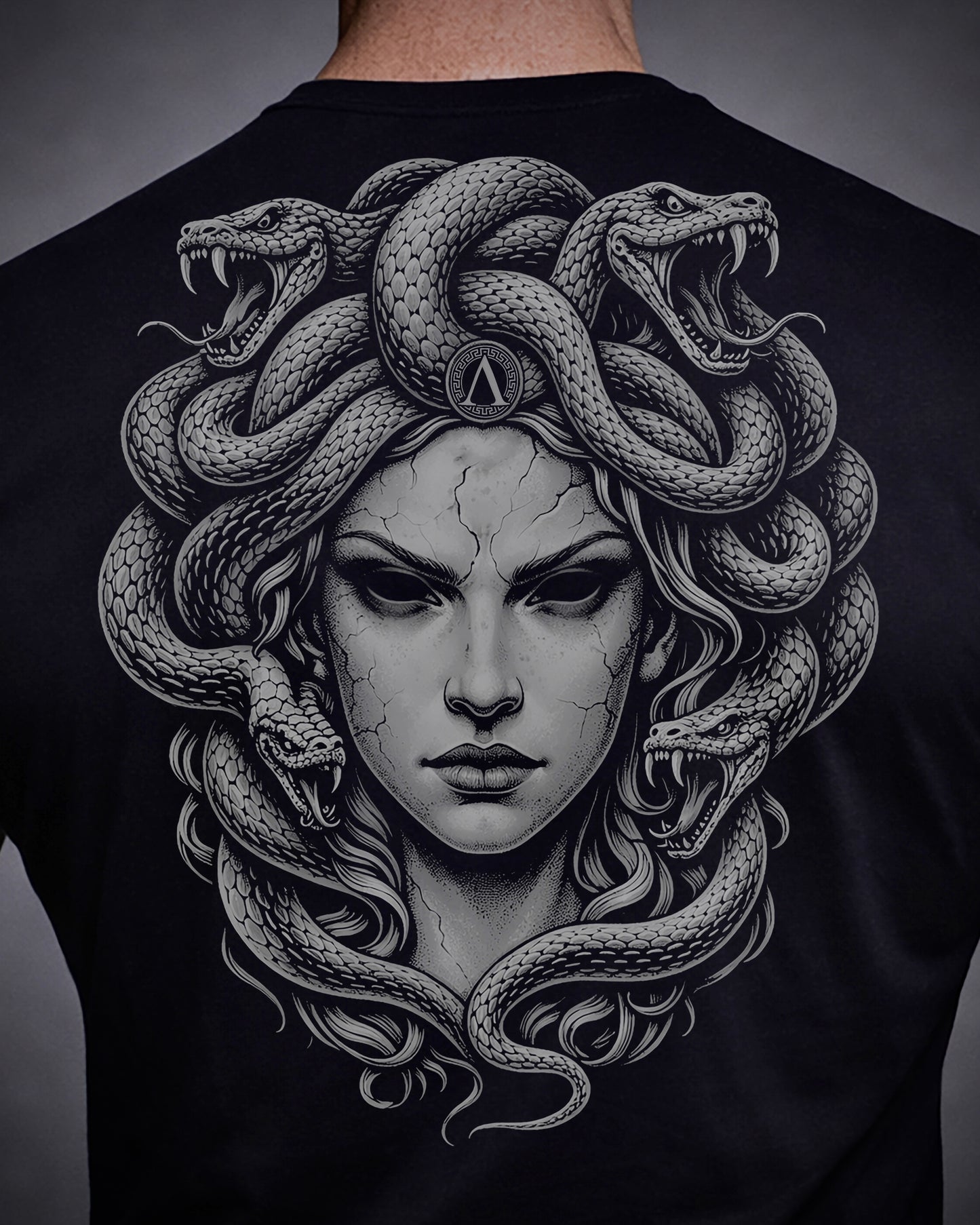 Close up of back view of man wearing black Achilles T-shirt printed with large Medusa logo on back