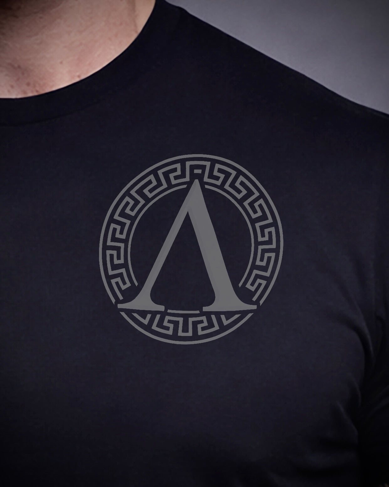Close up of front view of man wearing black Achilles T-shirt printed with roundel logo on chest