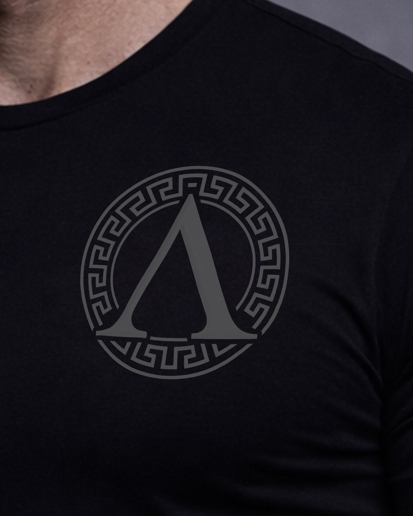 Close up of front view of man wearing black Achilles T-shirt printed with Roundel logo on front chest