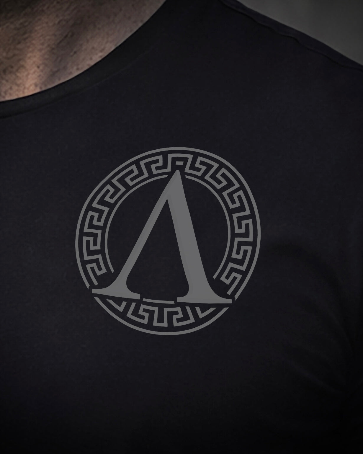 Close up of front view of man wearing black Achilles T-shirt printed with Roundel logo on front chest