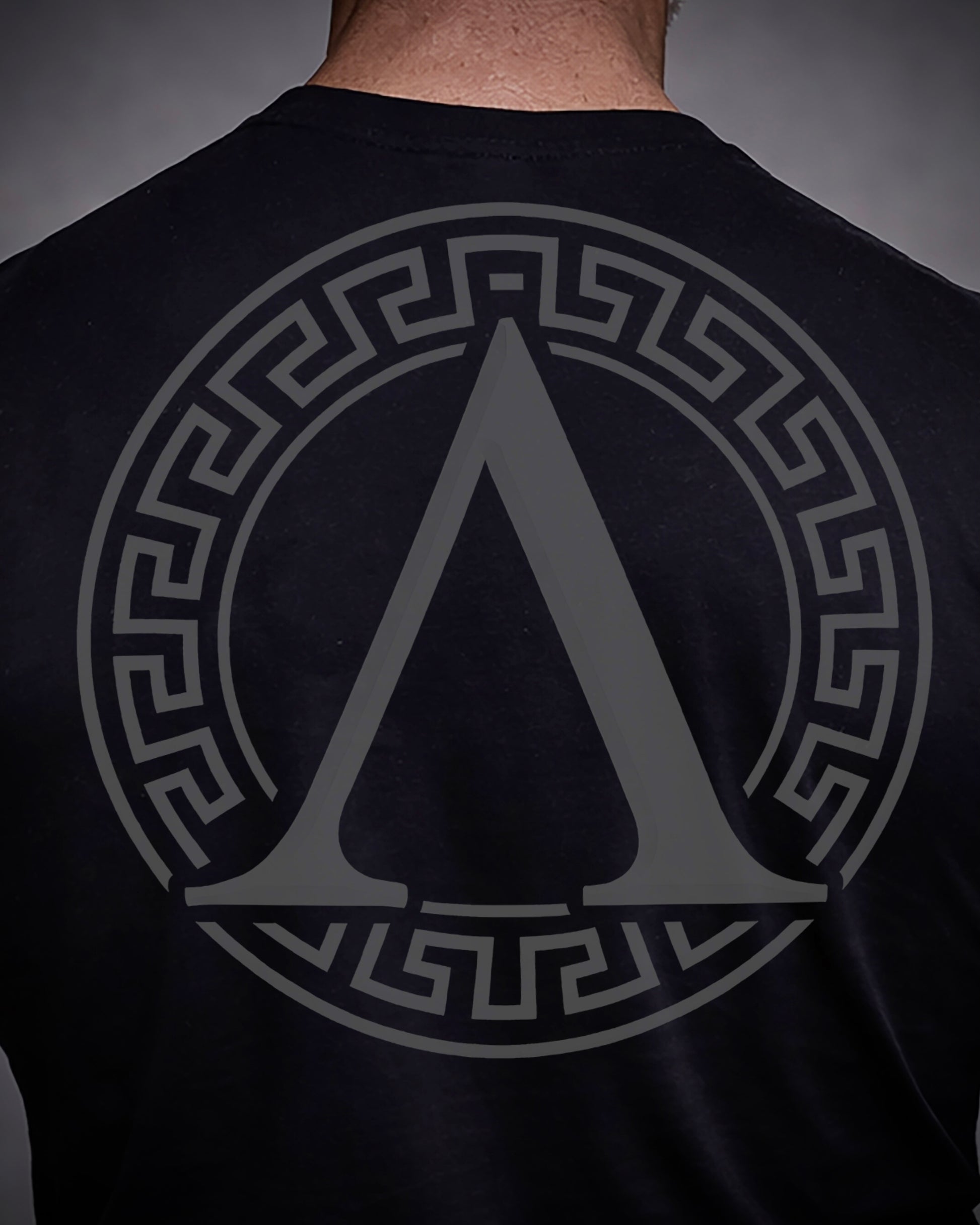 Close up of back view of man wearing black Achilles T-shirt printed with roundel logo on back