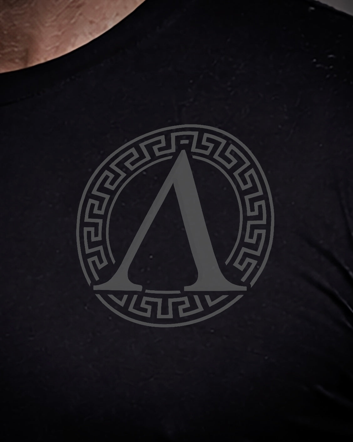 Close up of front view of man wearing black Achilles T-shirt printed with roundel logo on chest